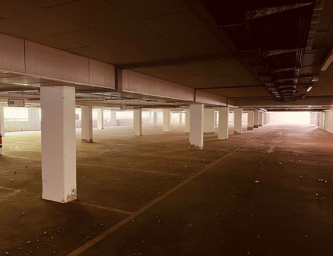 Garaje de Estacionamiento del Aeropuerto Sun Park – Estacionamiento subterráneo con columnas de concreto. Espacio vacío con espacios de estacionamiento visibles. La luz entra desde lejos.
