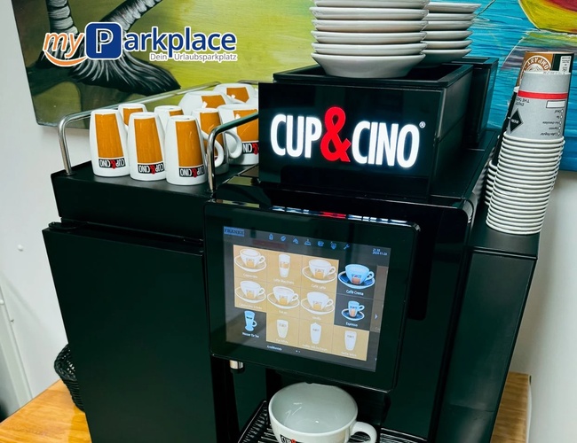 Parkovanie myParkplace – Kávovar s šálkami a pohárikmi. Dotyková obrazovka s výberom nápojov. Na stole stojí šálky.
