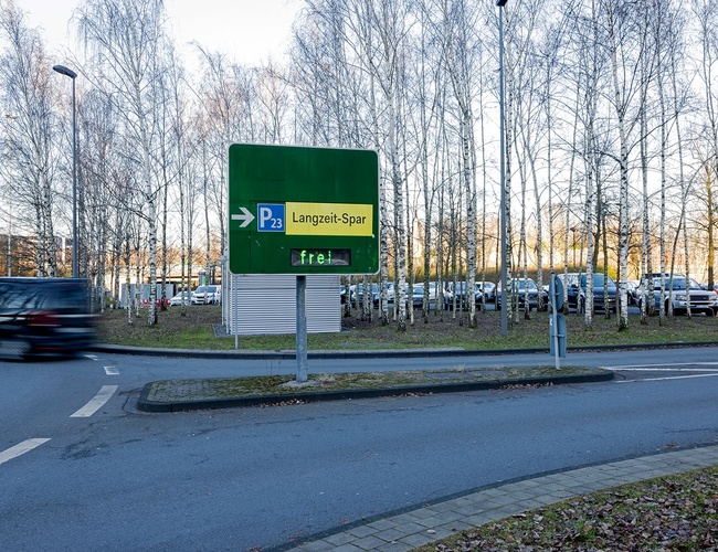 Droga prowadząca do parkingu P23 z dużą tablicą informacyjną oraz oznakowaniem kierującym ruchem pojazdów.
