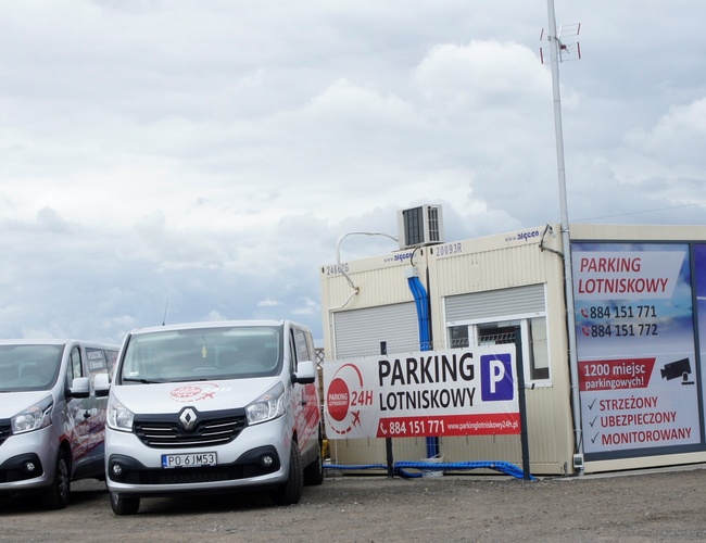 Parking Lotniskowy 24h - trzy minibusy stoją przed budynkiem. Na budynku duże reklamy. Parking jest ogrodzony i monitorowany.