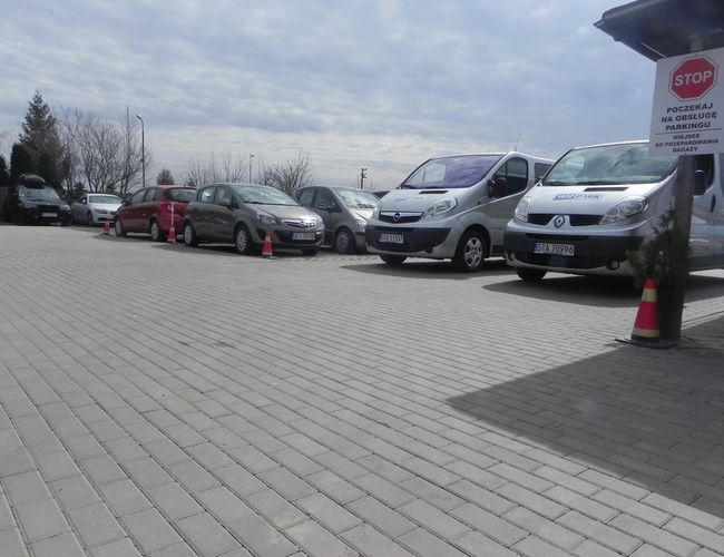 WIZ-PARK – Los coches están en fila sobre una superficie pavimentada. Están rodeados de conos bajos. Al lado se ve una señal de tráfico.