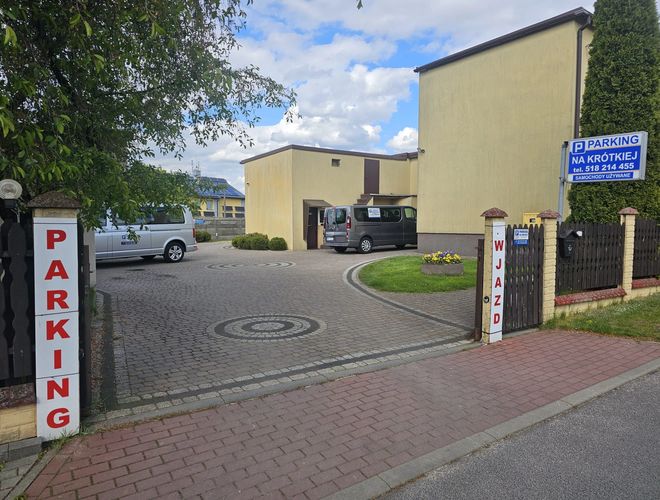 Parking na Krótkiej – Brama wjazdowa i tablica informacyjna. Na placu stoi biały samochód dostawczy. Na środku widoczny wzór na kostce.