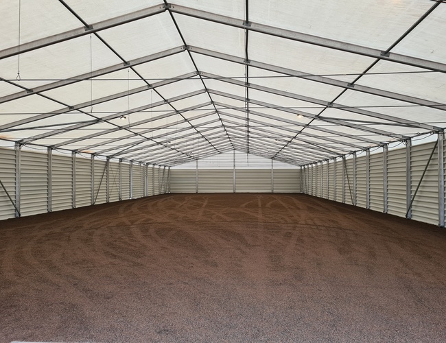 B1 Parkovanie zastrešené - Veľký, zakrytý priestor so štrkovým povrchom. Kovová konštrukcia podopiera priehľadnú strechu. Žiadne vozidlá.