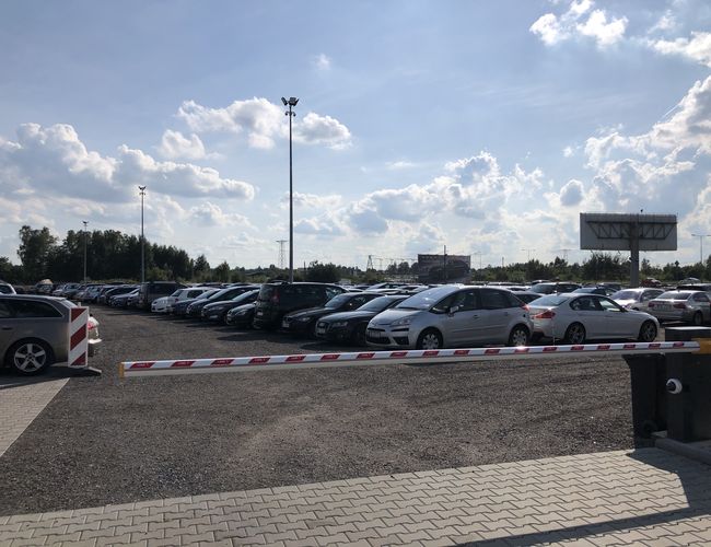 Parking A1 Rondo - Na zdjęciu widnieje plac z samochodami. Jest szlaban wjazdowy i wysokie latarnie. Teren jest nieogrodzony.