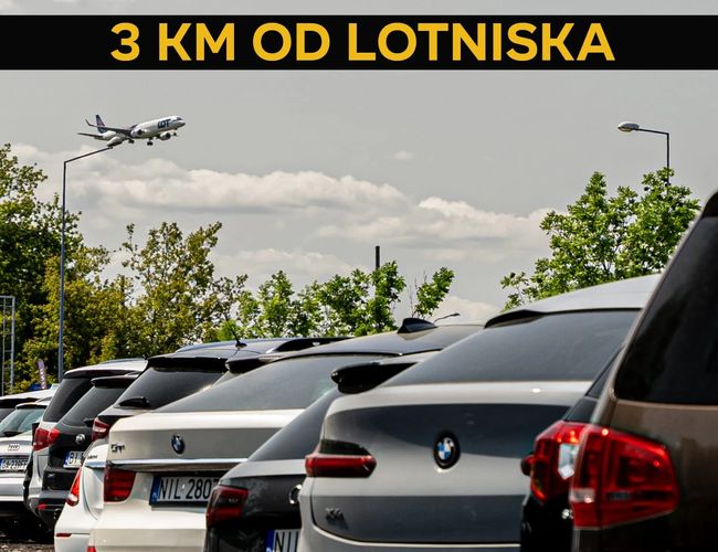 VIP Parking - przy trasie S2. Zaparkowane samochody pod drzewami. Samolot przelatuje nad parkingiem.