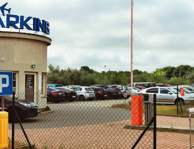 Günstiger und sicherer PREMIUM-Parkplatz – Umzäunter Parkplatz mit Schildern. Vollgeparkt, im Sommer von Grün umgeben.