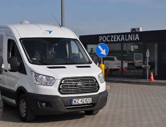 Parking Lotnisko – Biały van stoi na utwardzonym placu. W tle widoczne wejście do poczekalni.