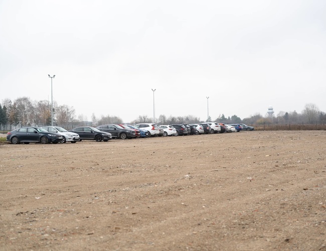 Jednoduché parkovanie štandard - Na obrázku je neupravené parkovisko. Niekoľko áut stojí v rade. Pozemok je oplotený sieťou.