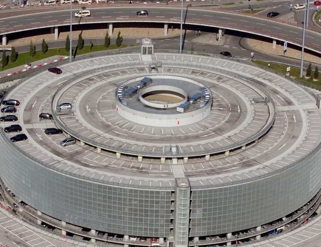 Widok z lotu ptaka na okrągły wielopoziomowy parking P2 z centralną rampą oraz drogami dojazdowymi otaczającymi obiekt.