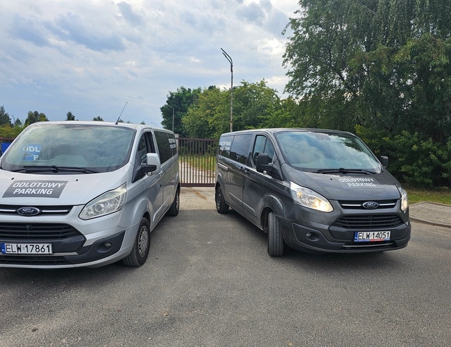 Odletové parkovisko Mado – pred bránou stoja dve dodávky. Pozemok je obklopený zeleňou a ohrádkou.