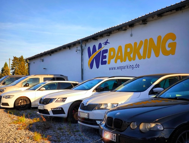 Zbliżenie na zaparkowane samochody przed budynkiem WE Parking z dużym logotypem na fasadzie.