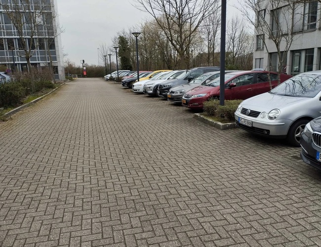 Sun Park Airport Parking Outdoor - Parking jest z kostki brukowej. Auta stoją w rzędzie przy budynku. Latarnie oświetlają teren.