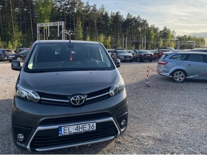 Auto Airport Parking – Duży parking na żwirowanej nawierzchni. Wiele zaparkowanych samochodów. W tle są drzewa.