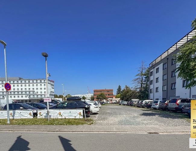 Parking Mein-Flughafenparkplatz-Frankfurt P3. Wjazd na teren parkingu przy dużym budynku, widoczne ogrodzenie i wyznaczone miejsca postojowe.