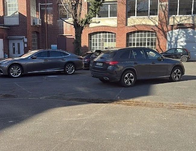 Parking Parkfinder24 Valet – Na parkingu stoją trzy samochody. Otoczenie jest z ceglanego budynku. Obszar jest częściowo zacieniony.