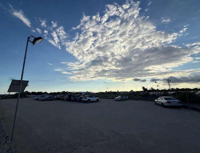 Duży parking o zmierzchu z rzędem zaparkowanych aut, latarnia uliczna i efektowne chmury na niebie.
