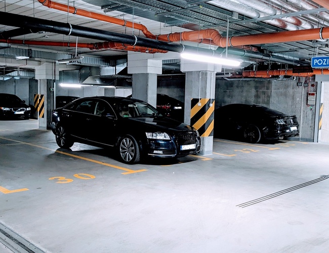 Odlet Garage - Podzemné parkovisko osvetlené neónovým svetlom. Automobily stoja na vyhradených miestach.