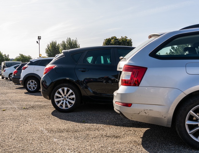Parking Letim Brno – kilka samochodów stoi na żwirowanym placu. Teren jest otwarty i nasłoneczniony. W tle rosną drzewa.