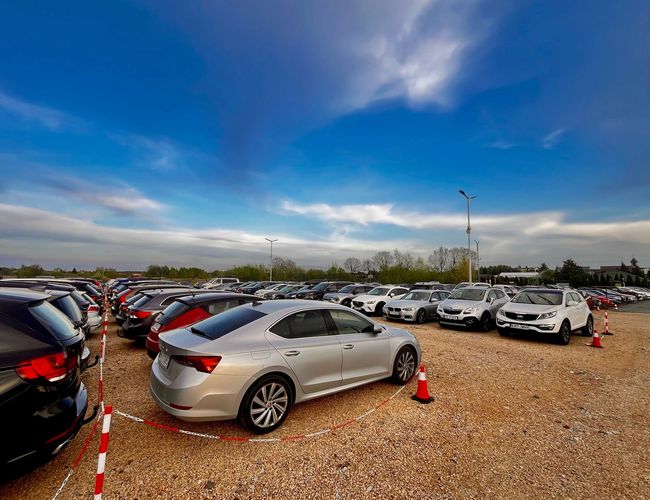 GoPark – Na parkingu stoją rzędy samochodów. Teren jest żwirowy i oświetlony latarniami.