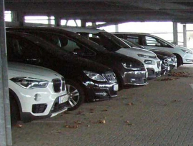 Паркінг Дюссельдорф з накритим паркувальником – Заштитована стоянка, багато припаркованих автомобілів. Покриття з бруківки. Частина автомобілів має видимі номерні знаки.