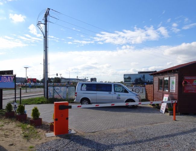 Ferietilgjengelighet Gdańsk - Parking med port og kontorbygning. På området står en lys bus parkert. Området er inngjerdet og velstelt.