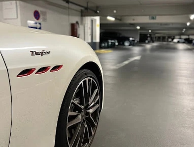 Parkolási Park2Travel Valet Garage – A fehér autó áll a garázsban. Látszik a kijárati tábla. Háttérként parkoló járművek sorai alkotják a hátteret.