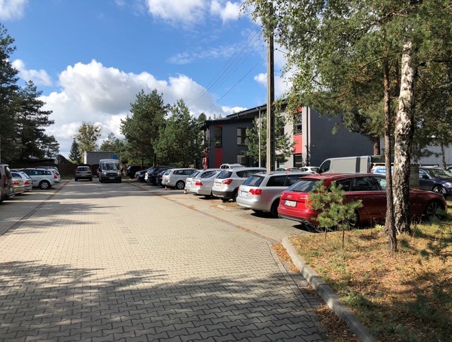 Puerto - En el aparcamiento hay coches estacionados. El entorno está arbolado. El terreno está pavimentado con adoquines.