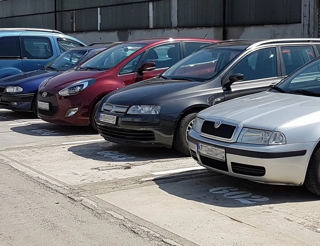 Parking z wieloma zaparkowanymi samochodami, widoczny rząd aut w różnych kolorach.