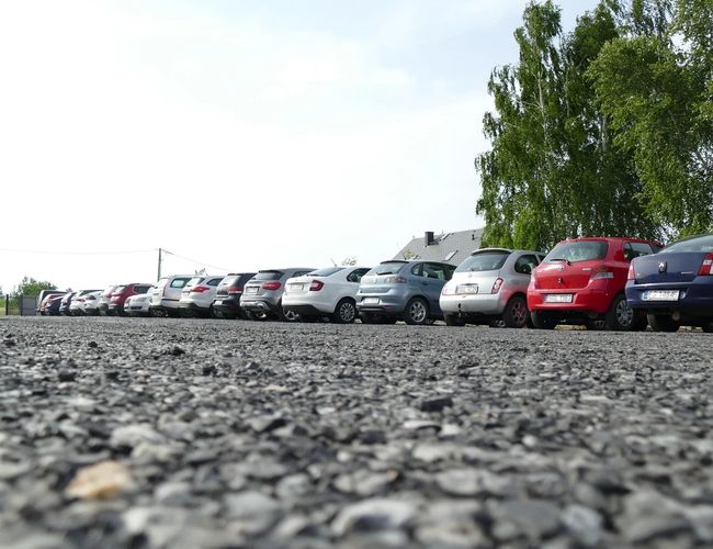 Diza Parking - Una fila de coches estacionados en un terreno de grava. El área está rodeada de árboles.