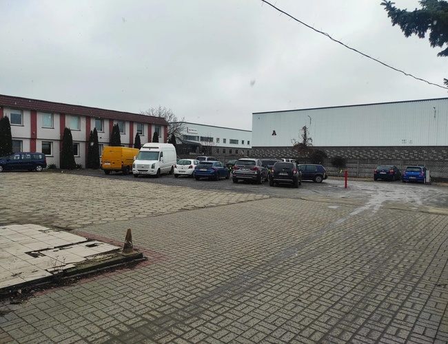 Parkovisko Šyšková 39 - Na dvorci stoja zaparkované autá. Na pozadí sú vidieť budovy. Pozemok je pokrytý dlažbou.