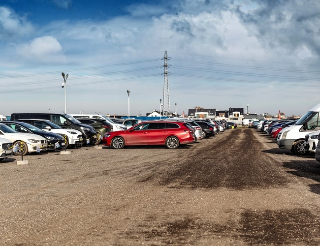 Parkovisko Okęcie Južné - rady áut na kamenistom povrchu. Parkovisko je otvorené, s osvetlením reflektormi.