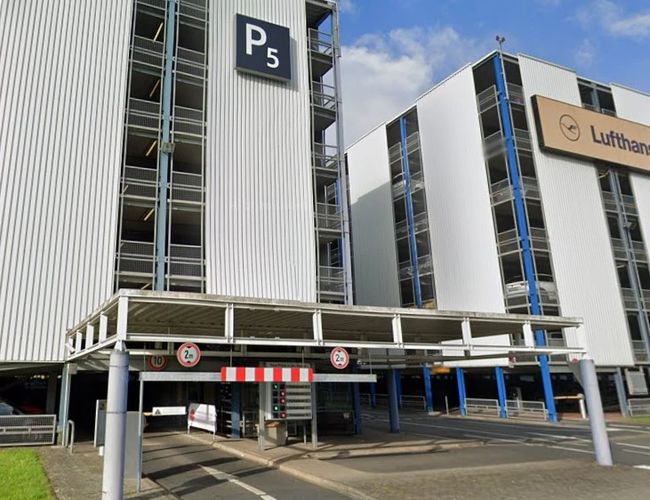Wielopoziomowy parking P5 z nowoczesną elewacją, oznakowanym wjazdem i dogodnym położeniem dla osób podróżujących samolotem.