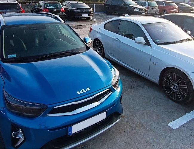 Parking Chopin - Na parkingu stoją dwa auta. Jedno jest niebieskie, drugie białe. Teren wydaje się otwarty.