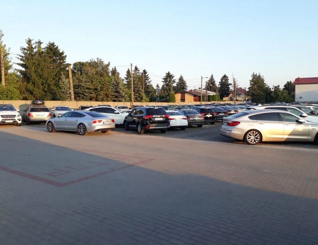 Parking P7 - Na placu stoją zaparkowane samochody. W tle widać drzewa. Parking jest częściowo zacieniony.