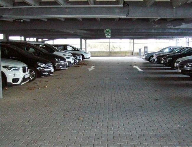 ParKing’s Düsseldorf Covered Valet – Zadaszony parking z samochodami zaparkowanymi po obu stronach. Betonowa nawierzchnia jest czysta i przestronna.