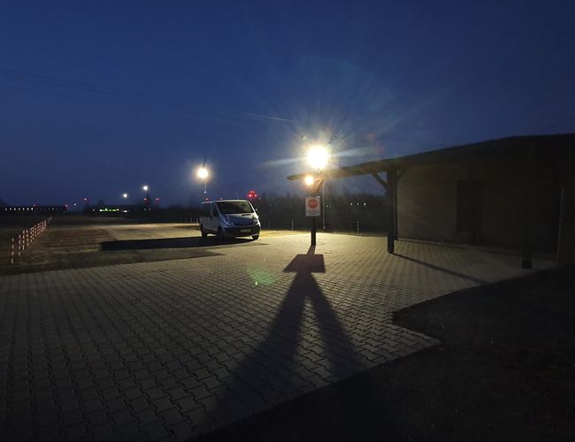 WIZ-PARK - Aparcamiento nocturno con iluminación. Un coche junto a la lámpara. Cielo oscuro de fondo.