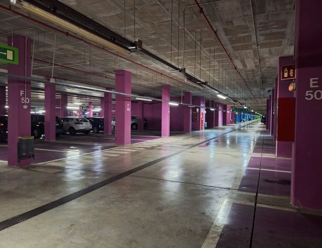 Parking Low Valet - wewnętrzny parking z fioletowymi kolumnami. Miejsca są dobrze oznaczone, a oświetlenie jest jasne.