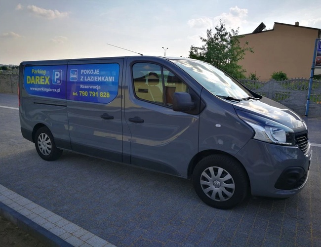 Aparcamiento Darex - Un furgón gris está estacionado en una superficie pavimentada. En el costado se puede ver un anuncio con datos de contacto.