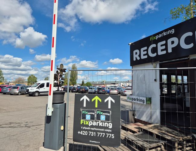 FixParking – Wjazd na parking z szlabanem i recepcją. W tle stoją zaparkowane auta pod błękitnym niebem.