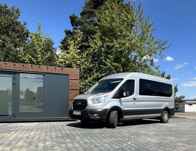 Inicia con nosotros – Hay una furgoneta plateada estacionada en el aparcamiento. Al lado hay un contenedor gris. En el fondo crecen árboles.