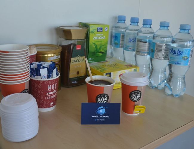 Royal Parking – stolik z kawą, herbatą i wodą. Obok leżą filiżanki i mieszadła. W tle stoją butelki wody.