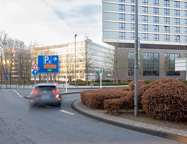 Oznakowanie parkingu P8 ustawione przy drodze dojazdowej z terminalem lotniska widocznym w tle.