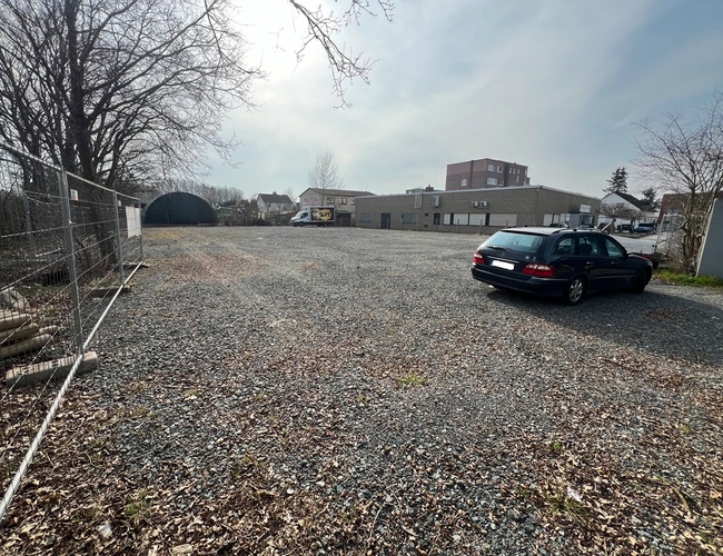 Parkovisko ParkPoint24 Valet - Miesto je štrkovité a nieohladené. Stojí na ňom jedno auto. V pozadí sú viditeľné budovy.