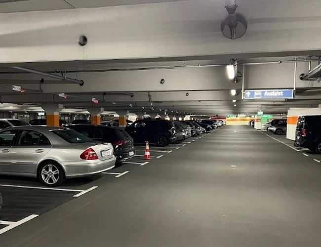 Hala parkingowa z rzędami zaparkowanych samochodów i oświetleniem sufitowym.