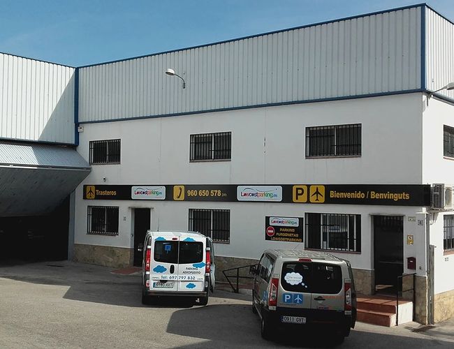 Lowcost Parkplatz Valencia – Gebäude mit weißer Fassade und großer Garage. Auf dem Parkplatz stehen zwei Lieferwagen.