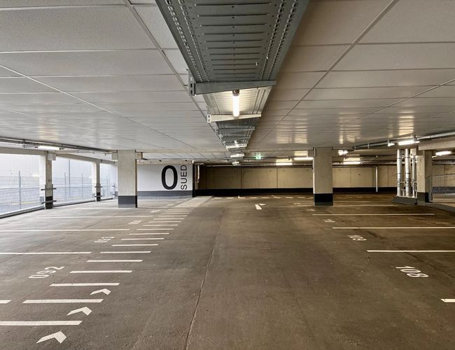 Parking Flughafenparker Valet - Zamknięta przestrzeń parkingowa z betonowymi filarami. Linia miejsc parkingowych oznaczona na podłodze. Oświetlenie sufitowe.