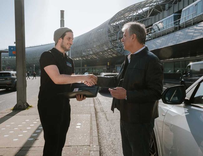 Parking Parkinsel24 VALET - Dwóch mężczyzn podaje sobie ręce. Obok stoi biały samochód. W tle widać nowoczesny budynek.
