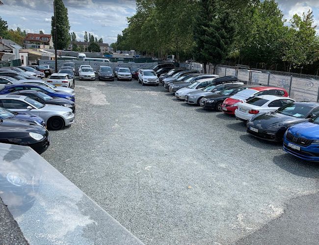 Parkovisko Parkparadies – Na námestí stojí veľa áut v dvoch radoch. Areál je otvorený a obklopený stromami a plotom.