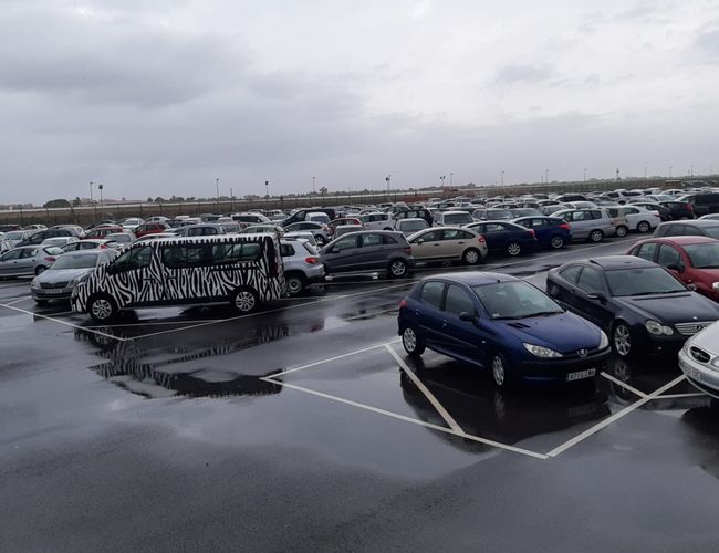 Victoria Parking Walencja - Deszczowy dzień na parkingu z zaparkowanymi autami. Widoczny pojazd z zebrą na boku. Teren jest ogrodzony.