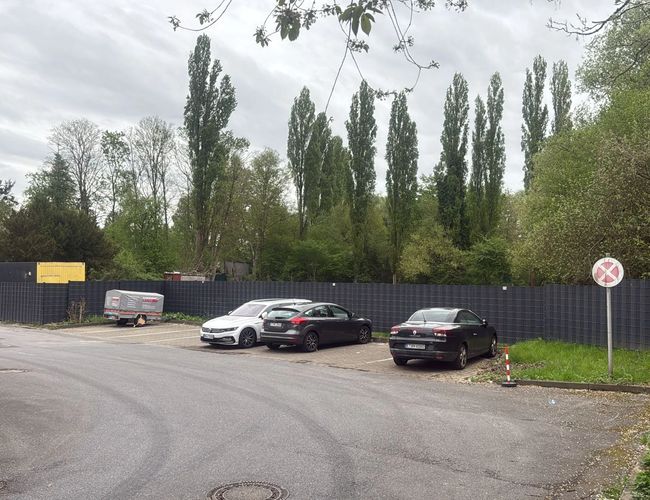 Parking Trust Park Fly - Parking jest ogrodzony metalowym płotem. Na terenie stoją trzy samochody. Widać także znak zakazu zatrzymywania.